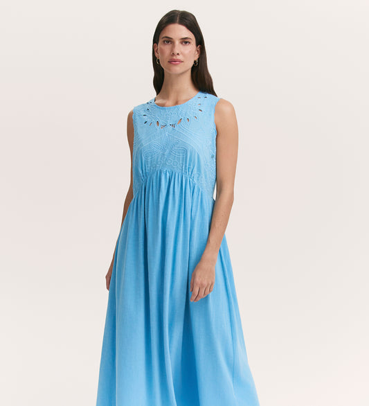 A woman with long dark hair wears the Liberte Light Blue Cotton Sleeveless Midi Dress, featuring an embroidered cut work bodice and intricate detailing, standing against a plain light background.