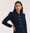 A woman with long, wavy dark hair models the Lucia Navy Crepe Midi Dress, which features long sleeves, a classic collar, and decorative front buttons. She poses with one hand on her hip against a plain background.