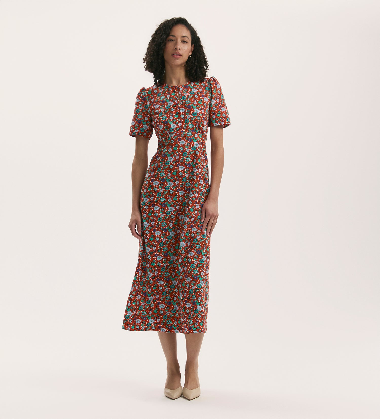 A woman stands against a plain background in the Marie Red Ditsy Crepe Midi Tea Dress, featuring short sleeves and crease-free crepe fabric, paired with beige pointed-toe shoes.