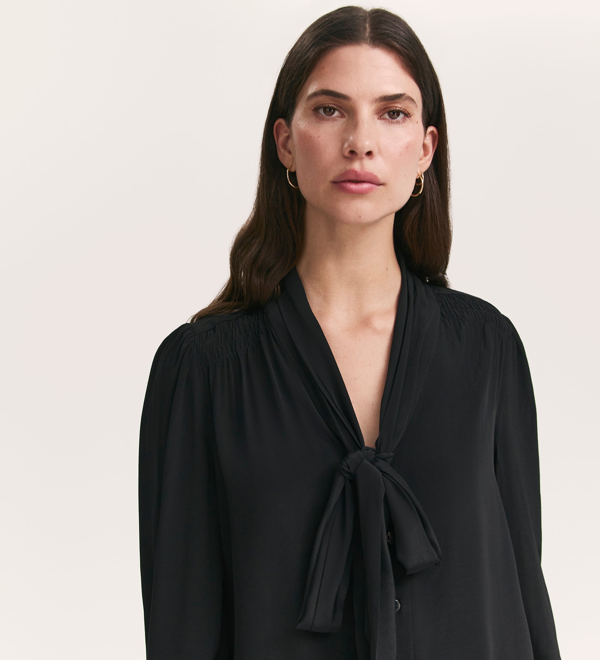 A woman with long dark hair wears the Mavis Black Chiffon Blouse, standing against a plain light background and looking directly at the camera.