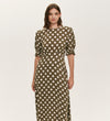 A woman stands against a plain light background wearing the Mela Khaki Polka Dot Midi Dress, featuring white polka dots, short puffed sleeves, and a flattering empire line waist.