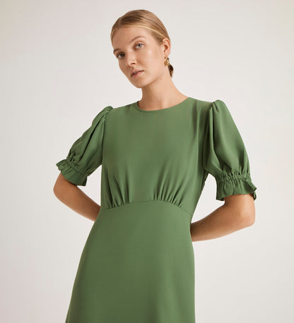 A woman wearing the Mela Green Chiffon Midi Tea Dress with puffed short sleeves stands against a plain light background, gazing slightly to the side with a neutral expression.