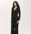 A woman with long curly hair wears the Melly Black Ponte Jersey Jumpsuit featuring wide-leg trousers and a V-neck, standing against a plain light background and looking ahead with a neutral expression.