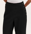 A person wears Nellie Black Canvas Wide Leg Trousers featuring decorative buttons along the waistband, paired with a white top. The image is cropped just below the chest.
