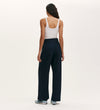 A person with long dark hair, seen from behind against a plain light background, wears a white tank top, light blue sneakers, and the Nellie Navy Canvas Wide Leg Trousers—a true wardrobe staple.