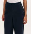 A person wears Nellie Navy Canvas Wide Leg Trousers featuring two rows of black buttons near the pockets, paired with a white top. The image focuses on the waist and upper legs.