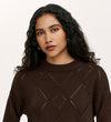 A woman with long, curly dark hair and gold hoop earrings wears the Odette Mole Knitted Jumper, standing against a plain light background and looking directly at the camera with a neutral expression.