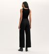 A woman faces away from the camera, wearing Olive Black Canvas Wide Leg Trousers with a sleeveless black top and ankle boots against a plain light background—an effortless elevated casual look.