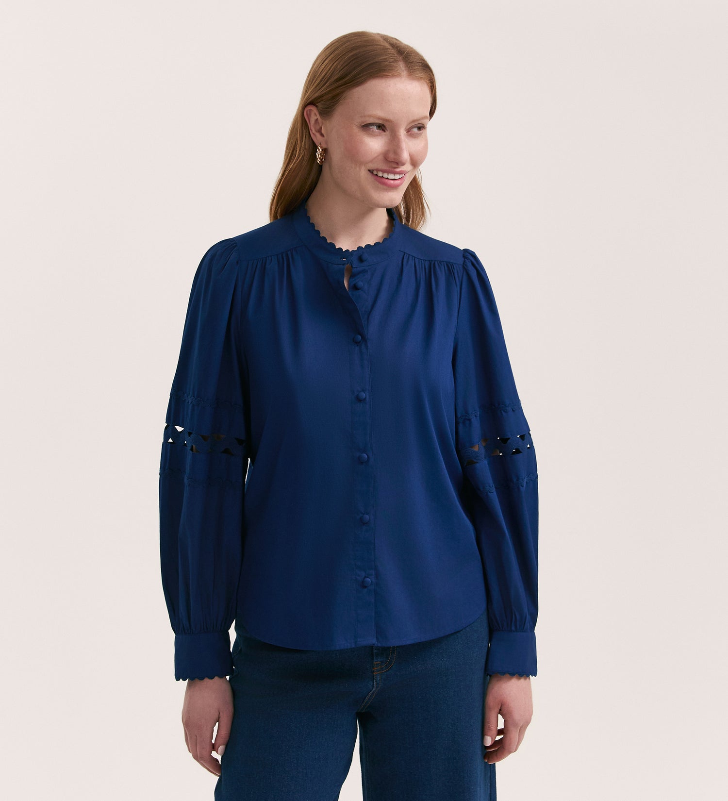 A woman with light brown hair, wearing the Paulie Indigo Cotton Shirt—a relaxed-fit button-up with ric-rac trim on the sleeves—and blue jeans, smiles against a plain light background.