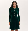 A woman stands against a plain light background wearing the Rae Bottle Green Velvet Short Dress, featuring long sleeves, a round neckline, and decorative buttons down the front.