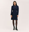 A woman stands facing forward in the Sabine Navy Crepe Short Dress— a woven crepe mini with long sleeves and a pointed collar—styled with black tights and ankle boots, set against a plain light background.