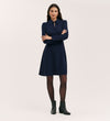 A woman stands with arms crossed, wearing the Sabine Navy Crepe Short Dress with a fitted cut and collar, paired with black tights and ankle boots, set against a plain light background.