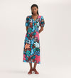 A woman wears the Sarah Blue Floral Crepe Midi Dress, featuring a V-neckline, short sleeves, and button-through front. Her straight hair and red strappy sandals complete the look against a plain light background.
