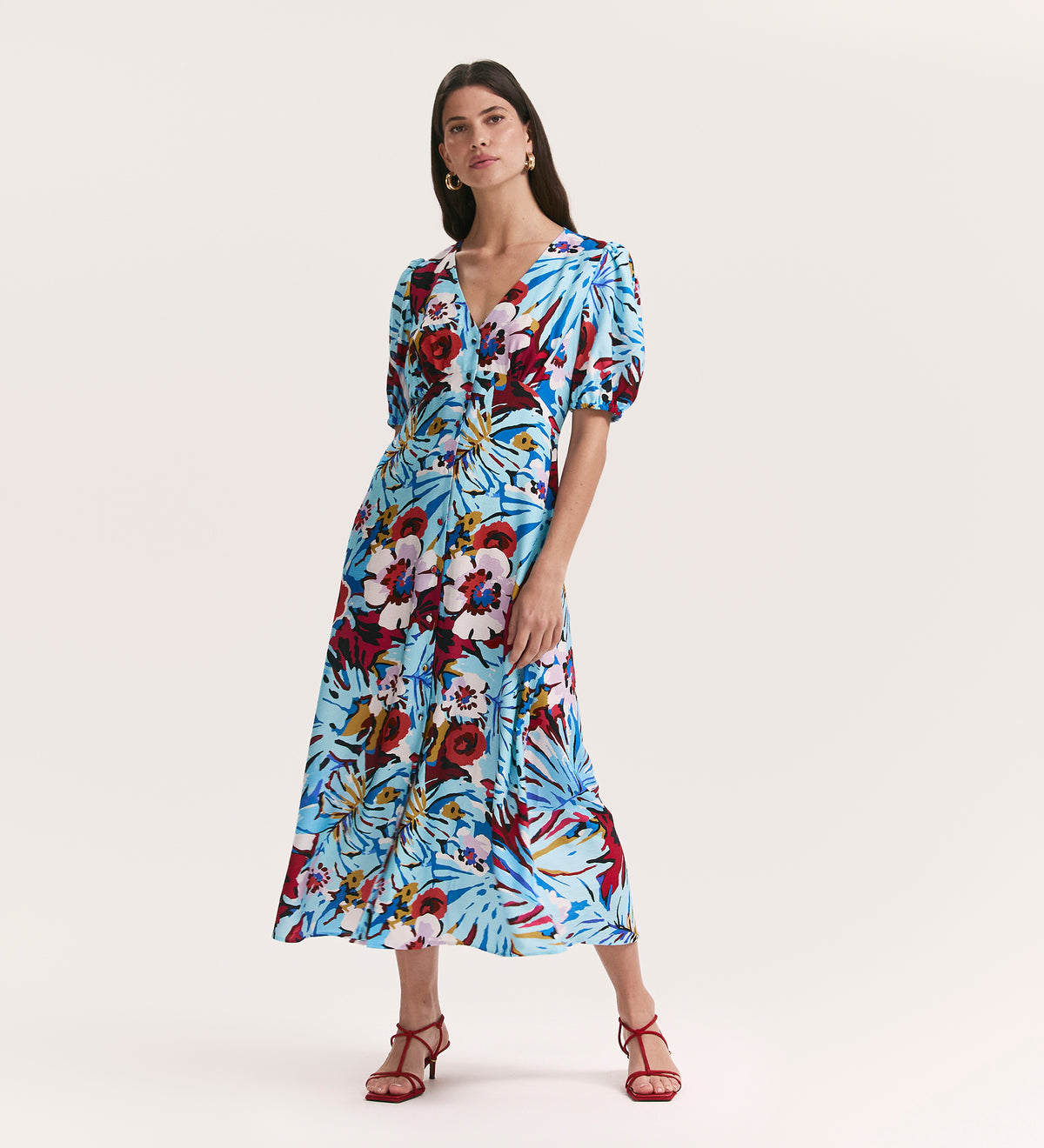 A woman wears the Sarah Aqua Floral Crepe Midi Dress with a v-neck, short puff sleeves, and red strappy heels against a plain light background.