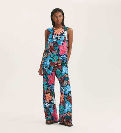 A woman poses against a white backdrop wearing the Eden Blue Floral Crepe Wide Leg Trousers, featuring a bold blue, red, pink, and white floral print on black with an elasticated waistband.