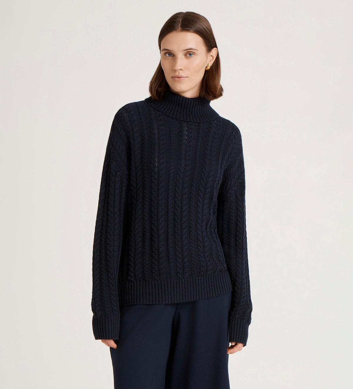 A woman with straight brown hair wears the Viviana Navy Knitted Jumper, styled with matching navy pants, standing against a plain light background.