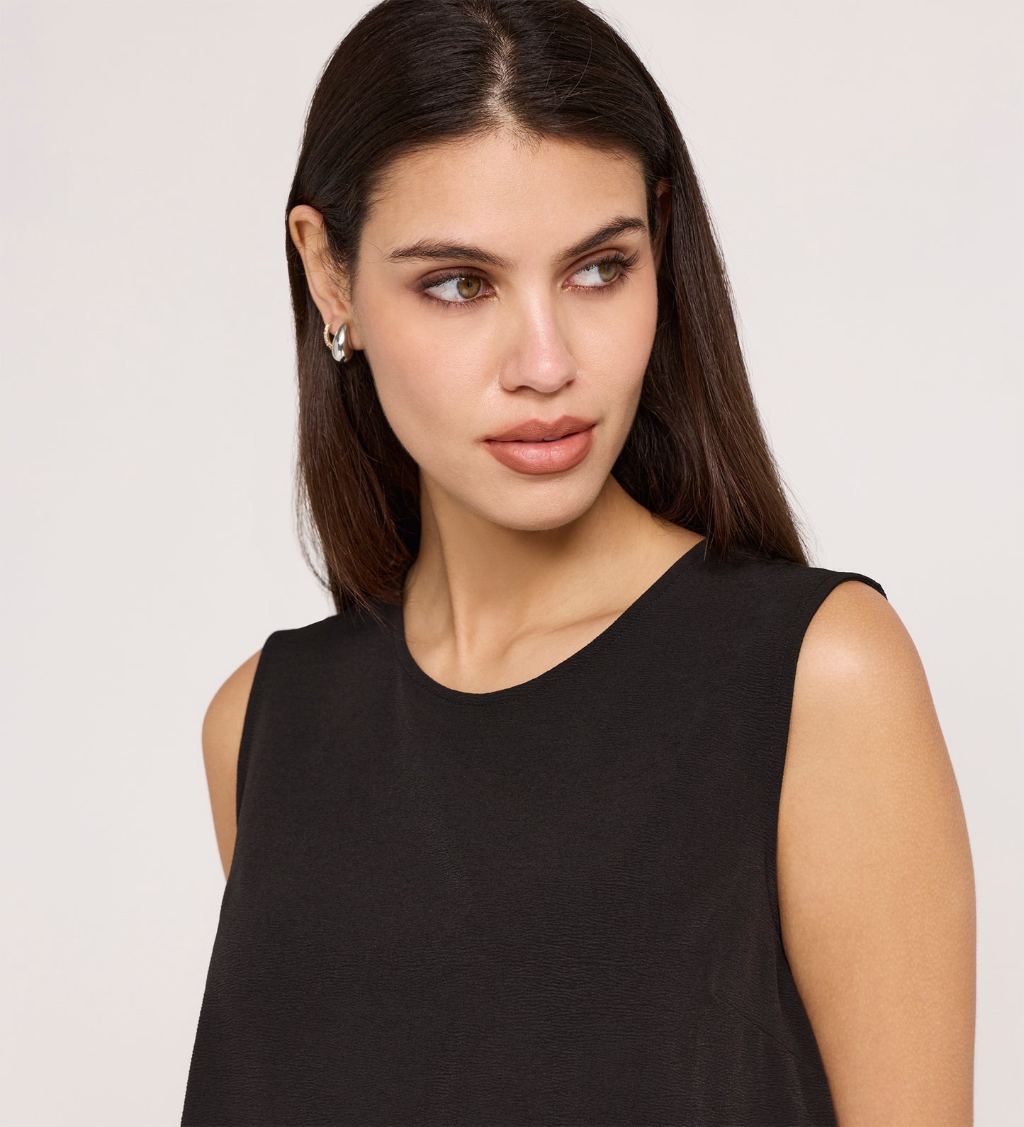 A woman with long dark hair, in small earrings and the Vallie Black Round Neck Vest—a relaxed fit, textured poly crinkle top—looks slightly to her right against a plain light background.