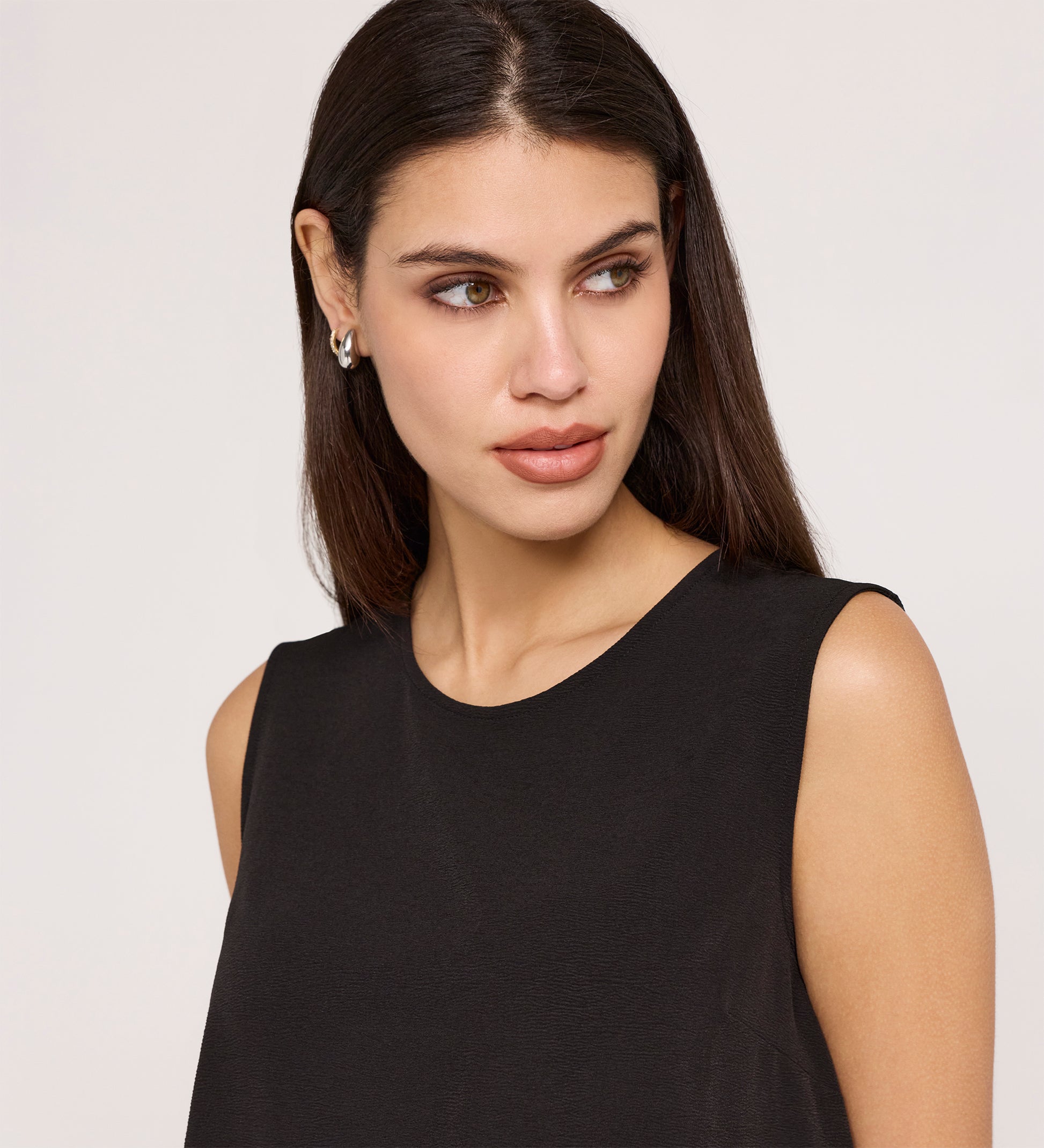 A woman with long dark hair, in small earrings and the Vallie Black Round Neck Vest—a relaxed fit, textured poly crinkle top—looks slightly to her right against a plain light background.