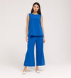 A woman with long dark hair stands against a plain background wearing the Vallie Cobalt Round Neck Vest in textured poly crinkle fabric, paired with matching blue wide-leg pants and white shoes.