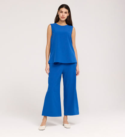 A woman with long dark hair stands against a plain background wearing the Vallie Cobalt Round Neck Vest in textured poly crinkle fabric, paired with matching blue wide-leg pants and white shoes.