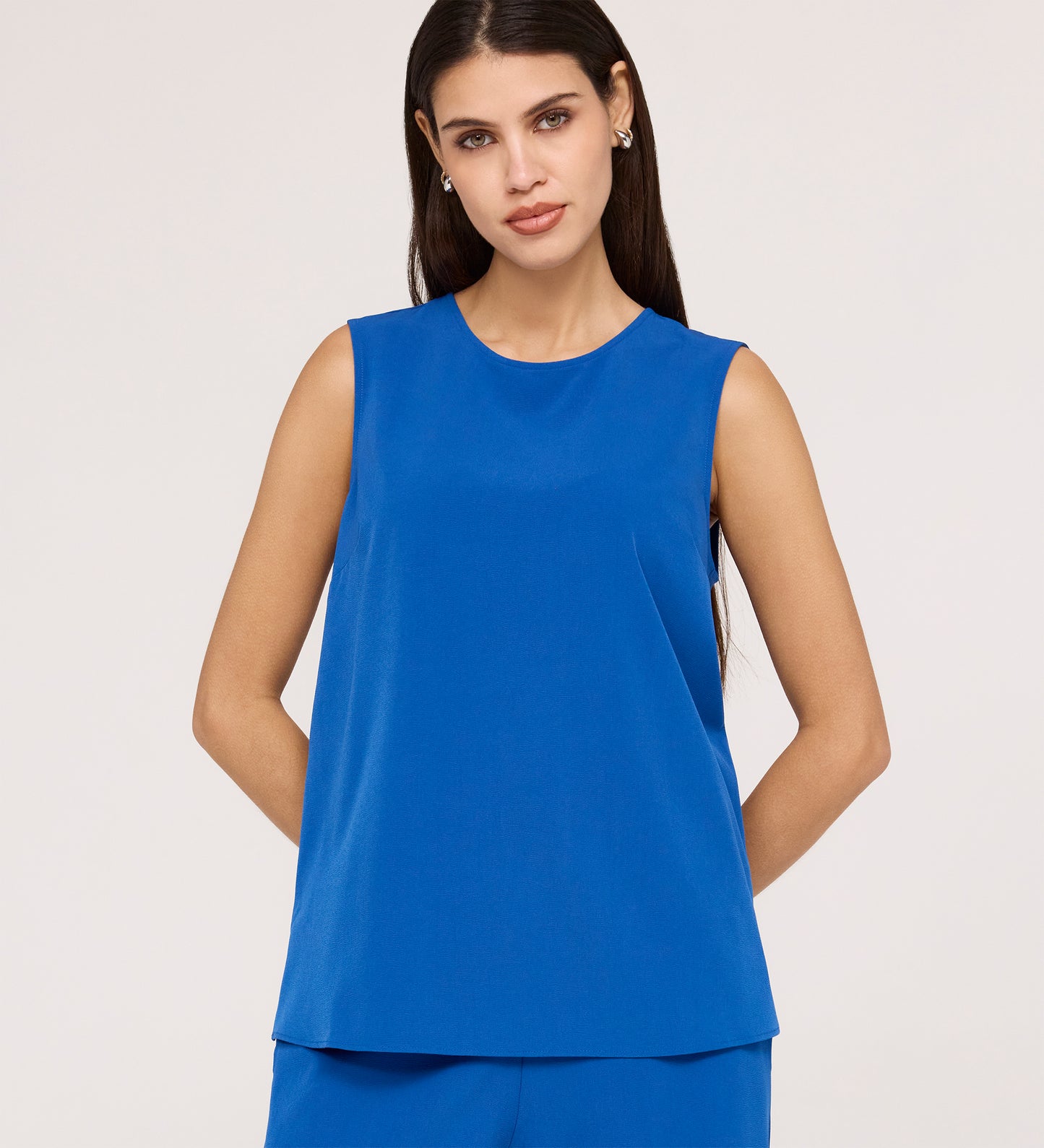 Woman with long dark hair wears the Vallie Cobalt Round Neck Vest and matching textured pants in bright blue, standing against a plain light background with her hands behind her back.