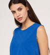 A woman with long dark hair and light eyes wears the Vallie Cobalt Round Neck Vest, a relaxed fit, sleeveless top in bright blue with subtle textured poly crinkle, standing against a plain light background and gazing softly at the camera.