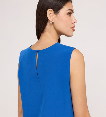Woman with straight dark hair wearing the Vallie Cobalt Round Neck Vest, a sleeveless textured poly crinkle top with a keyhole button detail on the upper back. Shown from the back and side against a plain, light-colored background.
