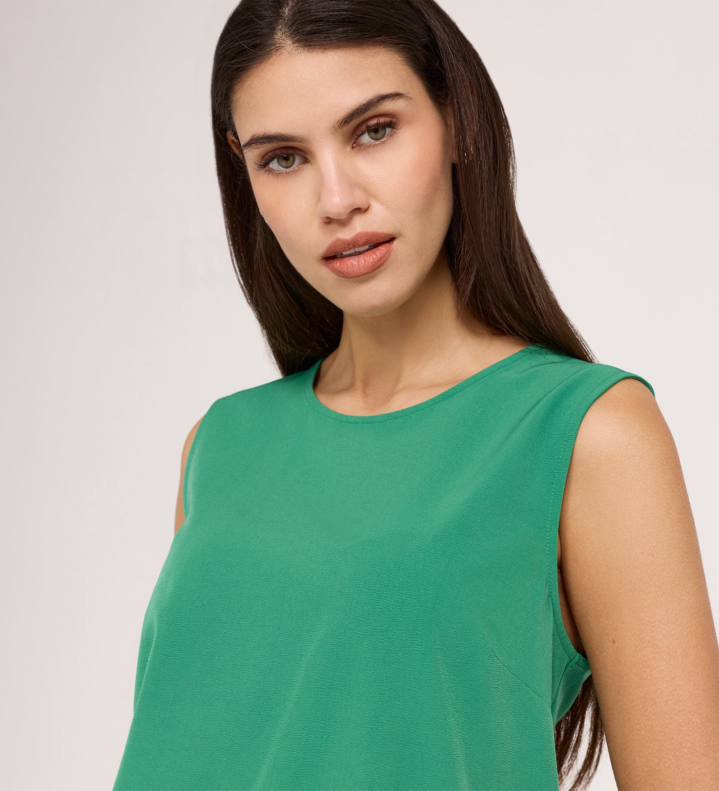 A woman with long dark hair wears the Vallie Green Round Neck Vest—a relaxed-fit, sleeveless top—and stands against a plain light background, gazing confidently at the camera.