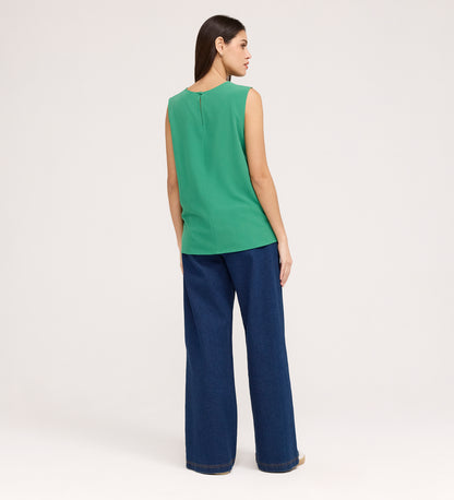 A woman with straight brown hair stands facing away, wearing the Vallie Green Round Neck Vest and wide-leg blue jeans against a plain light background.