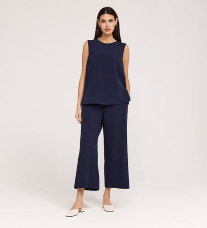A woman with straight dark hair and a neutral expression stands against a plain background, wearing the Vallie Navy Round Neck Vest in a relaxed fit, paired with matching wide-leg pants and white low-heeled shoes.
