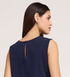 A woman with straight dark hair models the Vallie Navy Round Neck Vest in textured poly crinkle fabric, featuring a relaxed fit and back keyhole with button detail. She is shown from the back and side, wearing small silver earrings.