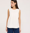 A woman with straight brown hair, wearing the Vallie Ivory Round Neck Vest and blue jeans, stands against a plain light background, looking to her left with a neutral expression.